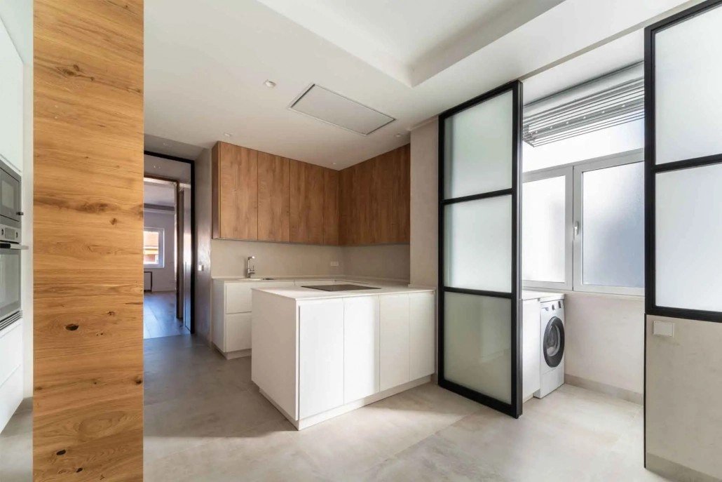 Cocina reformada con isla, muebles de madera y cerramiento de galería en aluminio negro